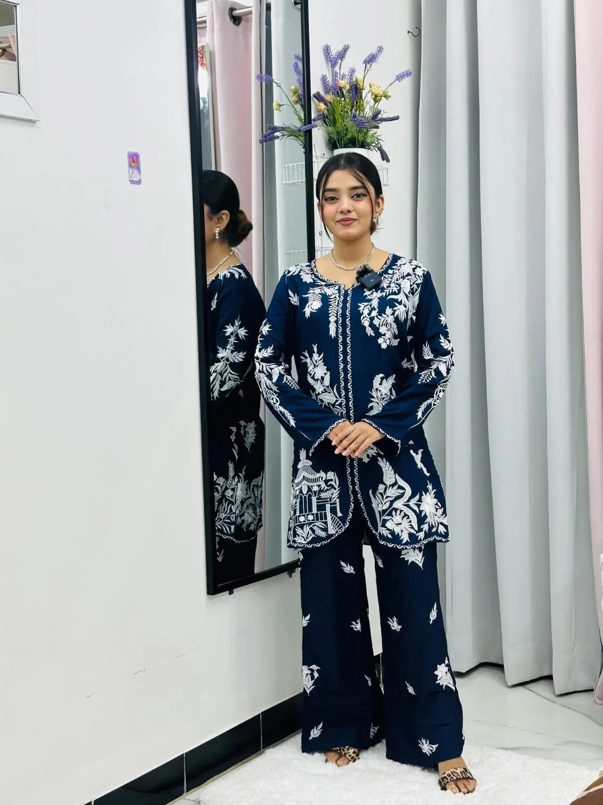 Woman in navy blue floral embroidered suit standing indoors near a mirror and curtains