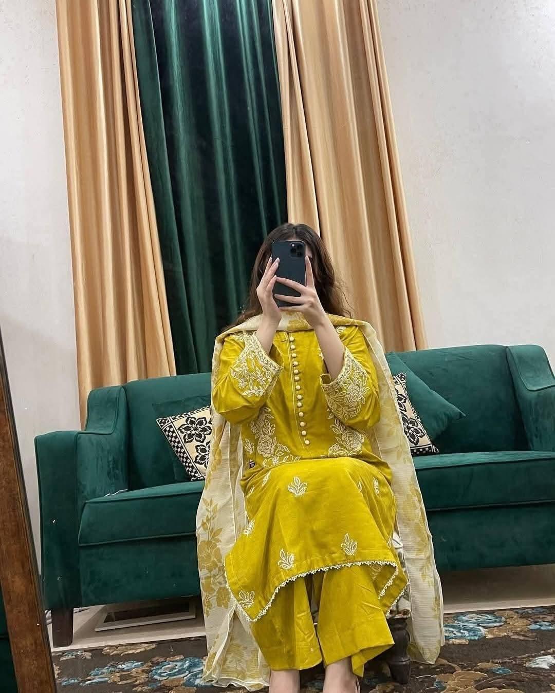 Woman in yellow embroidered traditional outfit sitting on green sofa taking mirror selfie