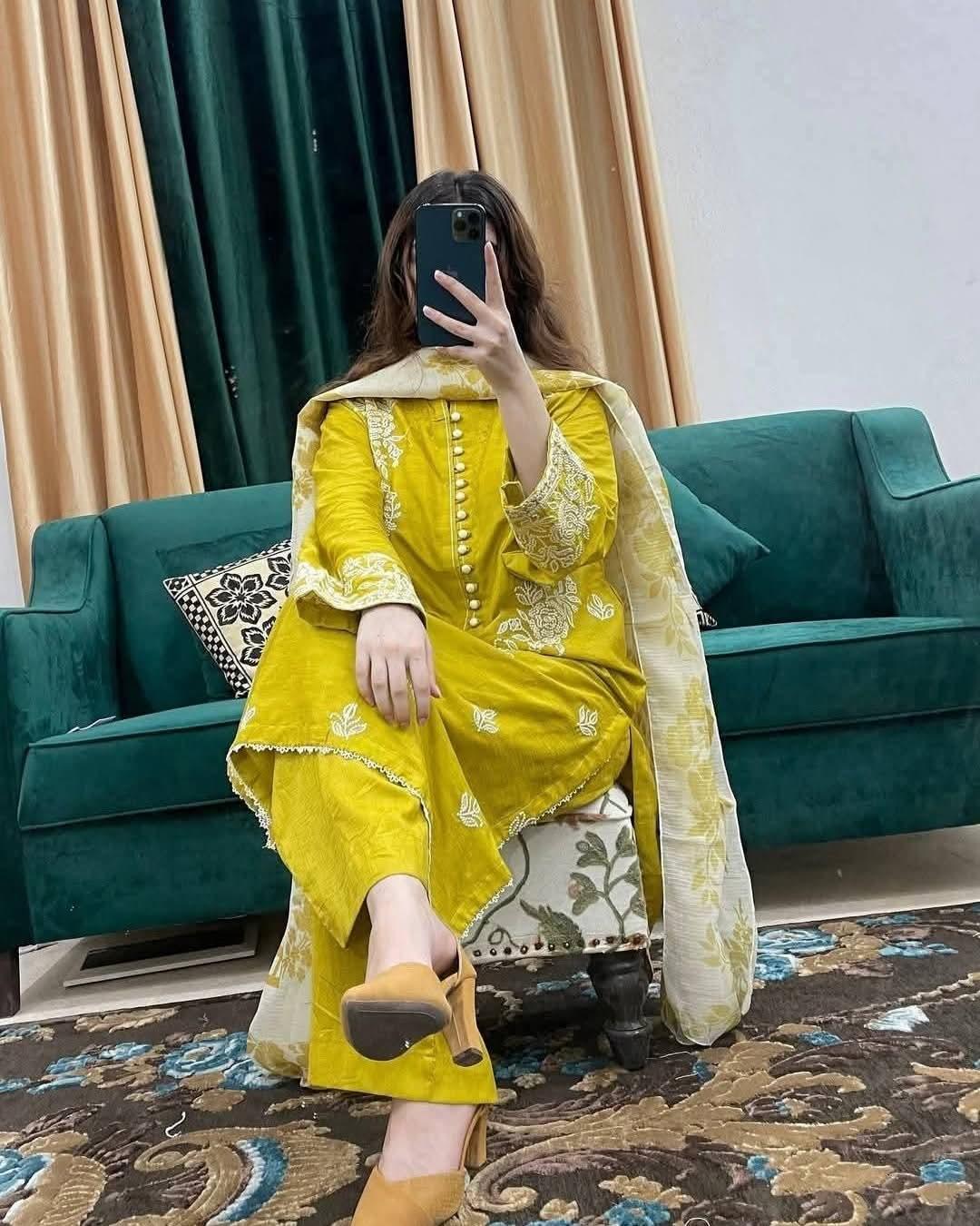 Woman in yellow embroidered traditional outfit with dupatta, sitting on green sofa indoors
