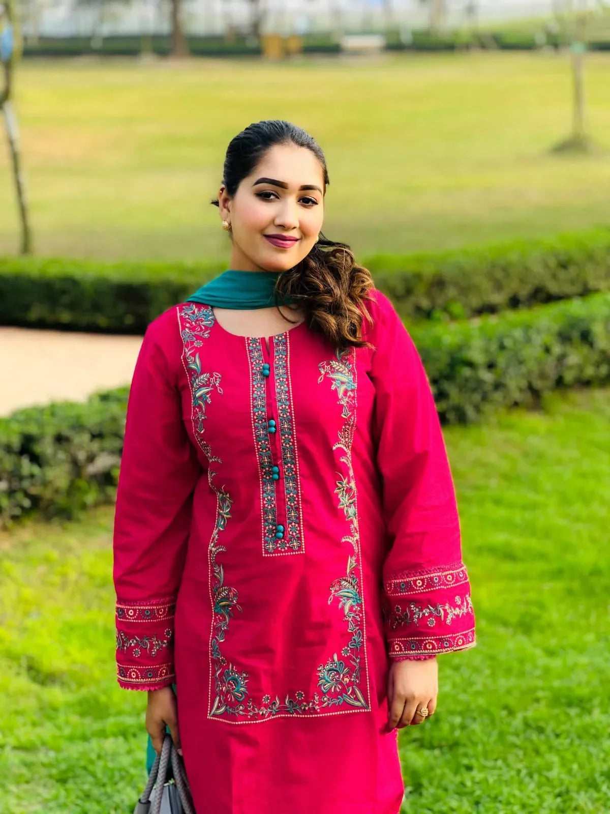 Woman in a pink embroidered kurta with teal dupatta standing in a garden